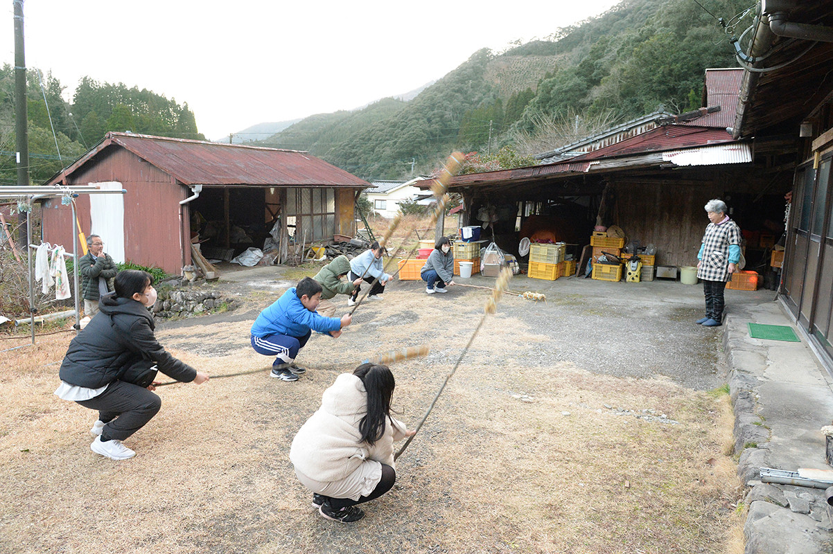 わら束を地面に打ち付け、もぐら打ちをする子どもたち
