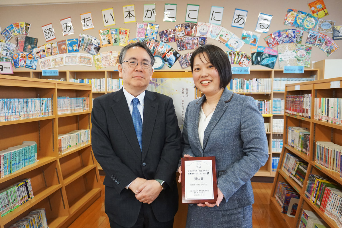 読書推せん文コンクール団体賞の表彰楯と一緒に写る中馬淳常務理事と畑田千香教諭