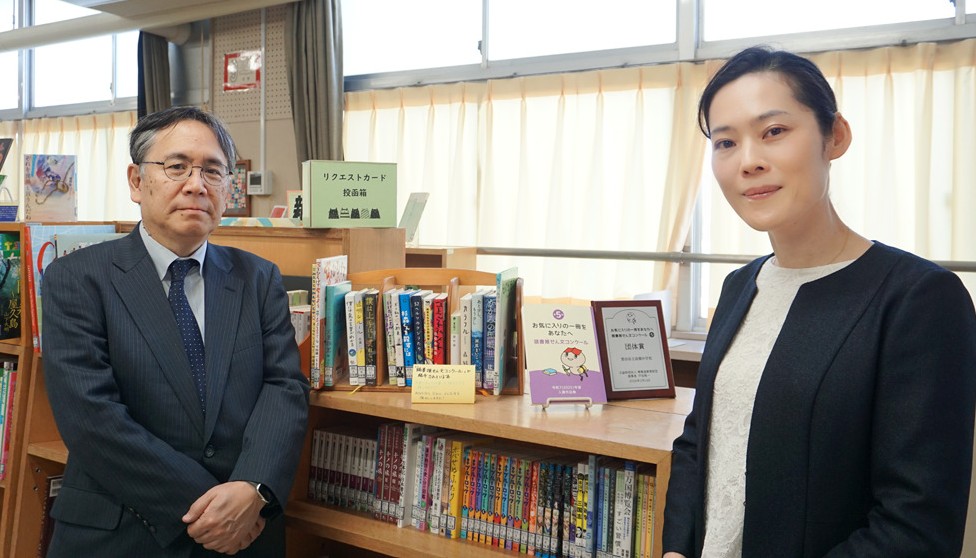 図書室入り口で写る中馬淳常務理事と岩月彩奈教諭