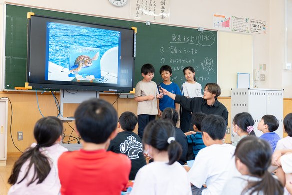 ウミガメの写真が映るスクリーンの発表に聞き入る子どもたち
