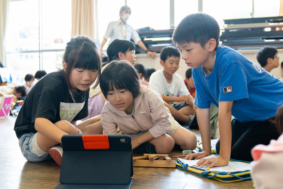 タブレットを囲んでどの写真を使うか話し合う子どもたち