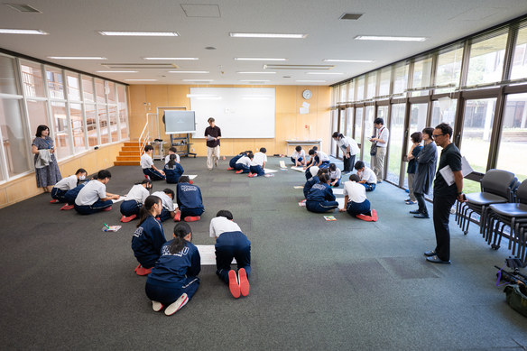 広い教室でグループごとに模造紙へ教訓を書き込む生徒たち