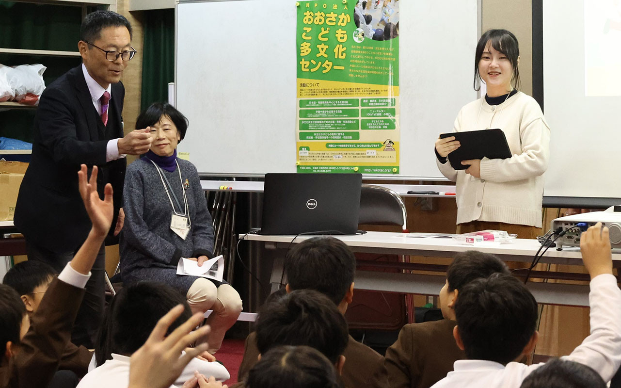 中国語で自己紹介する鄭婷婷さん（右）。左は糸井利則校長とオコタックの村上自子理事＝大阪市港区の市立磯路小